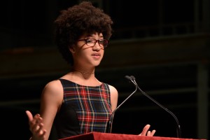 A teenaged girl stands behind a podium delivering a speech