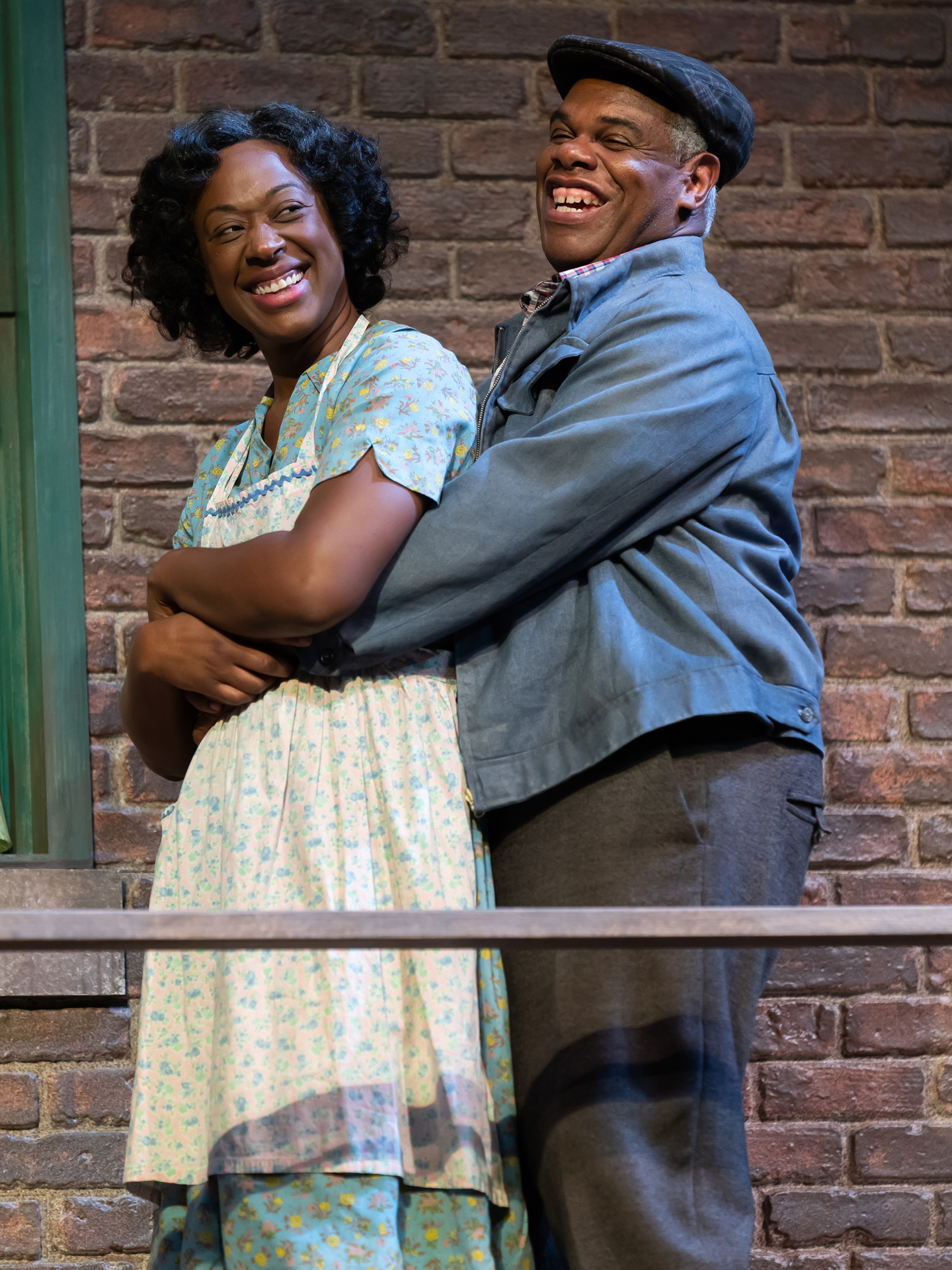A married couple stands on their porch smiling and embracing.