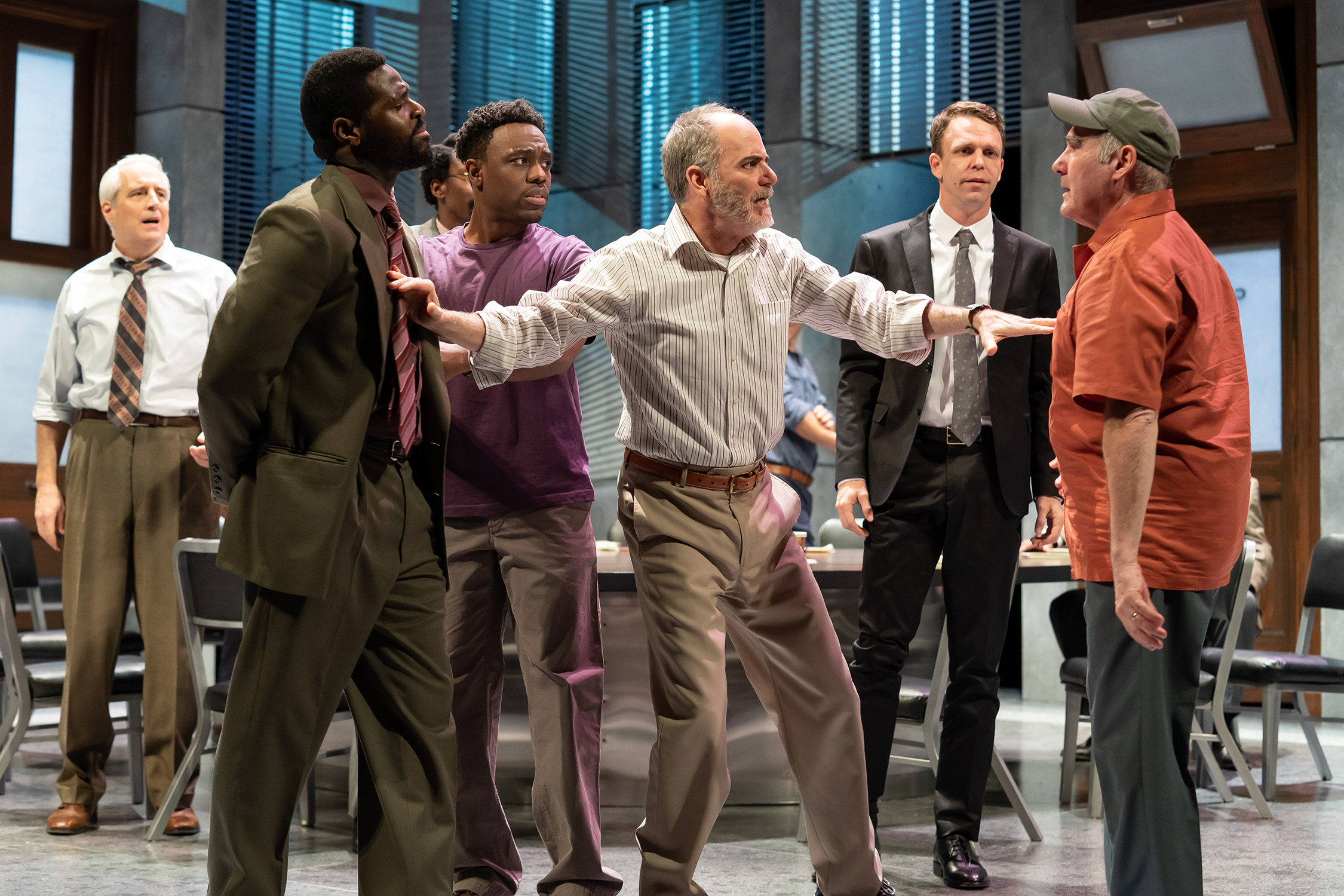 Six men stand in a jury room as heated words are exchanged between two jurors (actors Lawrence Redmond and Bueka Uwemedimo). A foreman (actor Eric Hissom) stands between the two men, attempting to deescalate the flight. Image is from the Ford’s Theatre 2019 production of Twelve Angry Men, directed by Sheldon Epps. Photo by Scott Suchman.