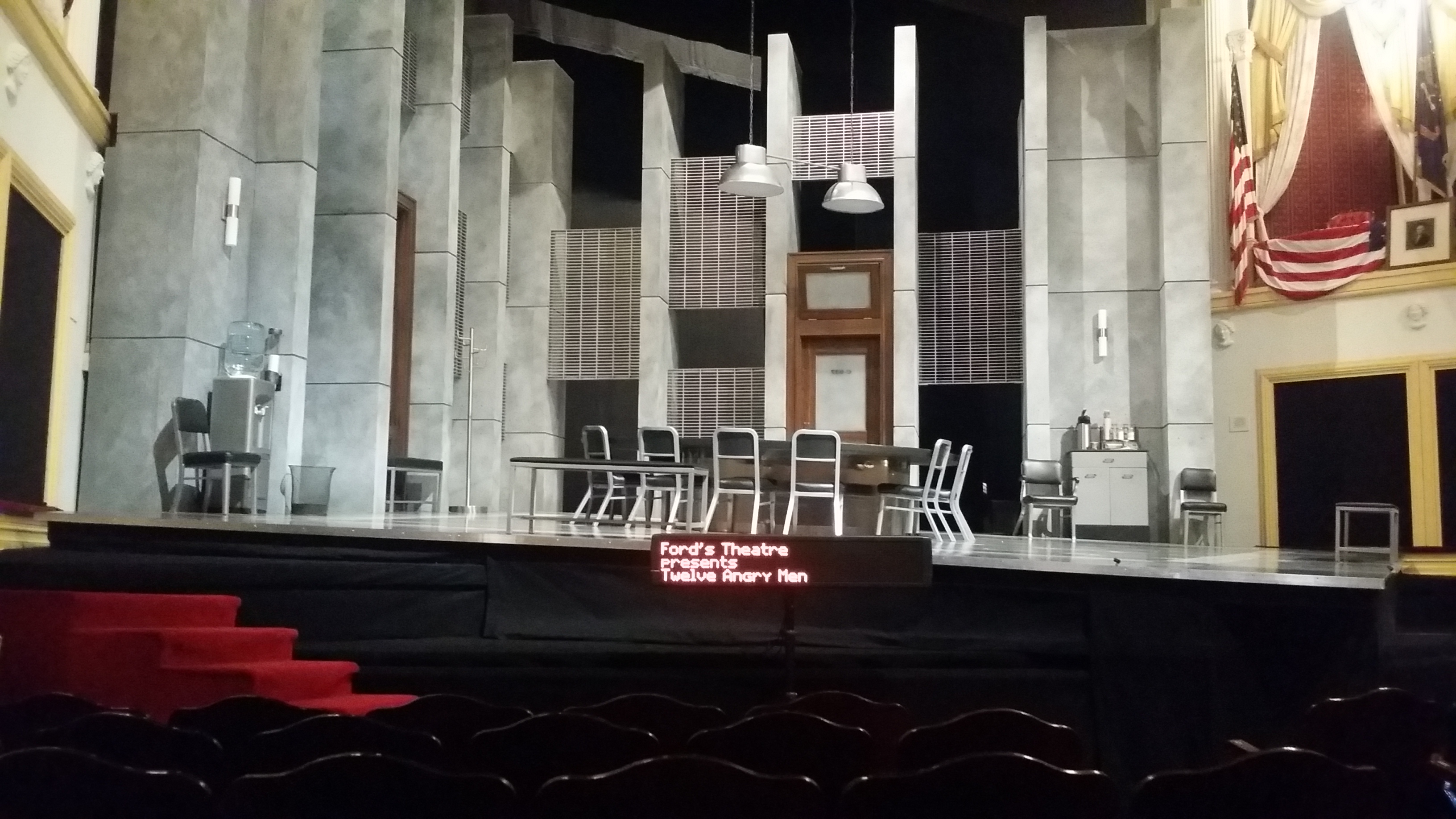 A captioning screen sits on the lip of the stage before a performance at Ford's Theatre. On it reads an opening message " Ford's Theatre presents 'Twelve Angry Men'"