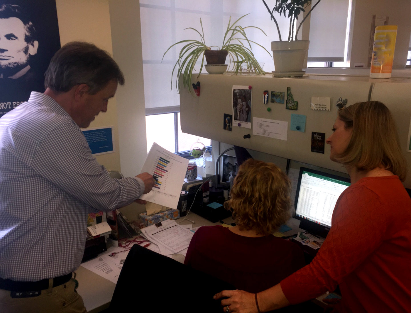 Three Ford's Theatre staff members gather around a computer screen looking at analytics charts.