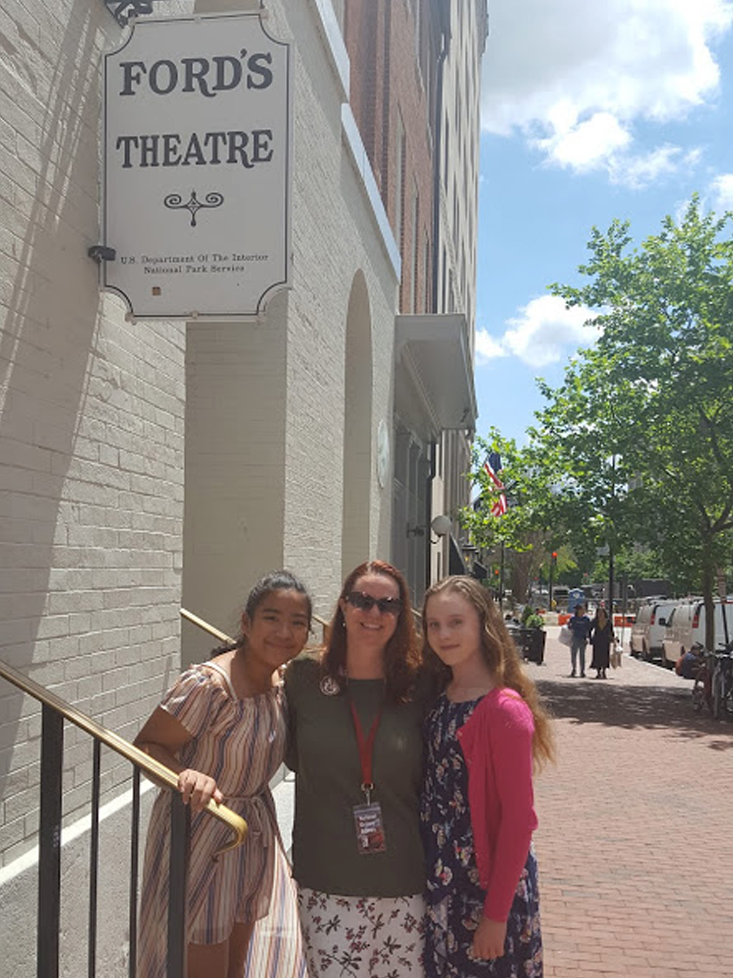 Teacher Karen Richey stands outdoors on the historic steps of Ford’s Theatre flanked by two of her high school students.