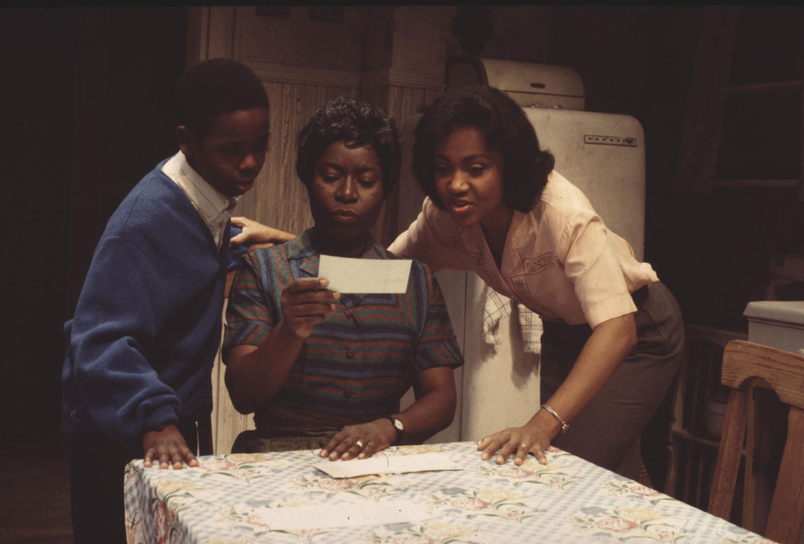 Photo of three actors in the 1995 Ford's production of "A Raisin in the Sun." The three are huddled at a kitchen table looking at a piece of paper.