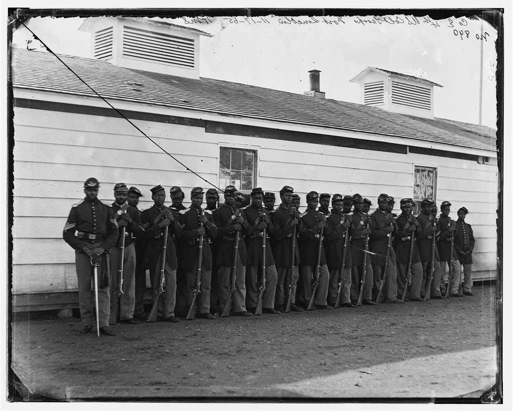 26 black Union soldiers in uniform stand in front of a building